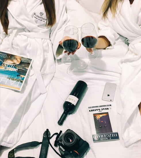 Top view of two friends holding glasses of wine and reading magazines at the hotel