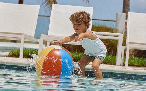 young boy reaching for beach ball in pool