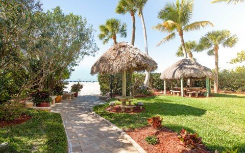 Brick path toward beach with tiki huts & palm trees 
