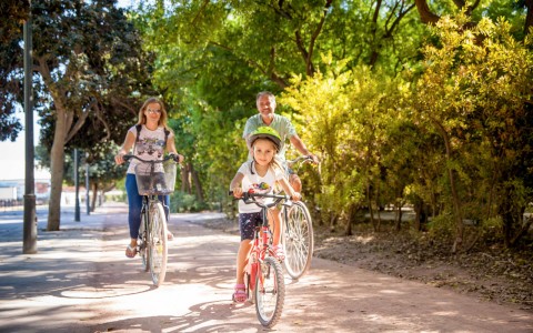 Couple & daughter riding bikes on path surrounded by trees 