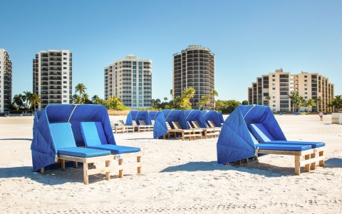 Blue loungers with umbrellas on sand with buildings in the back 