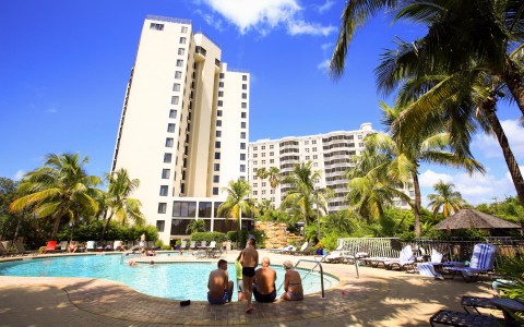Family sitting on pool side with hotel building in the back 