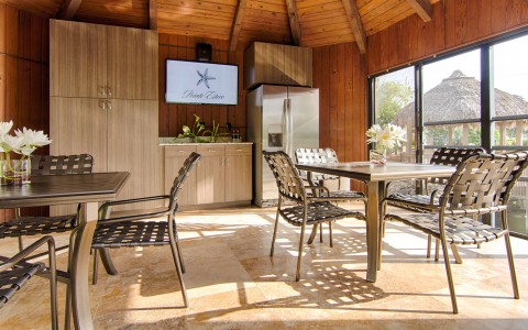 Dining lounge with metallic tables & chairs with window panel overlooking tiki hut & water 