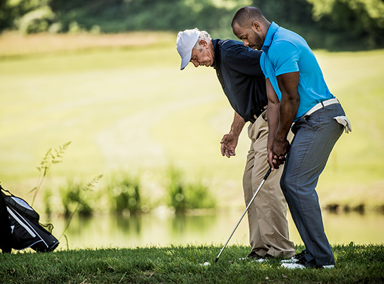 Old man teaching younger man how to hit golf ball 