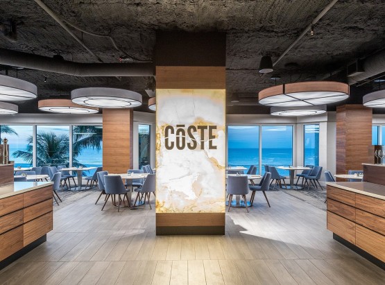 Restaurant with a column in the middle that says coste and blue chairs