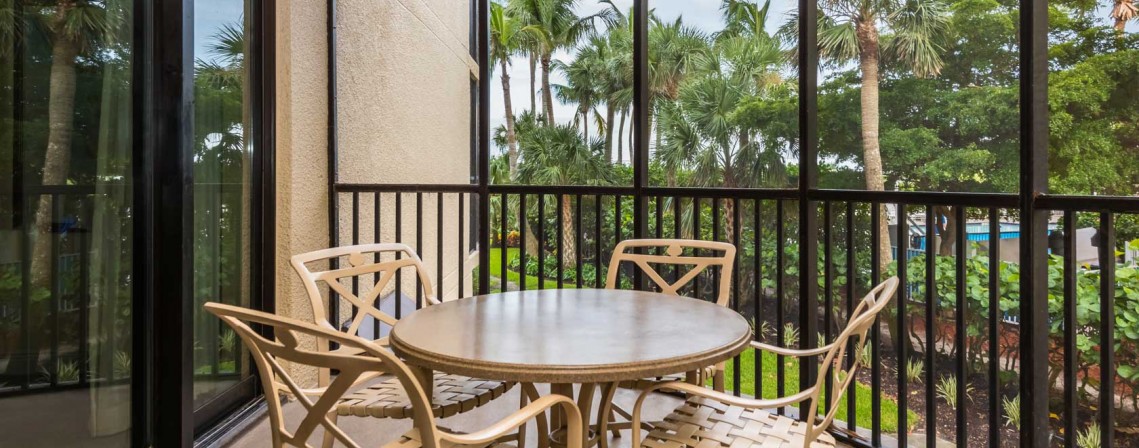 screened in balcony with table and four chairs with a view of luscious palm trees
