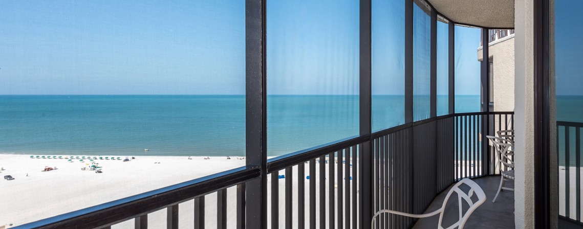 screened in balcony overlooking the ocean with chairs and side tables
