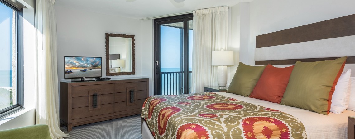 gulf view penthouse suite bedroom with a king size bed, dresser and sliding glass door leading to a balcony