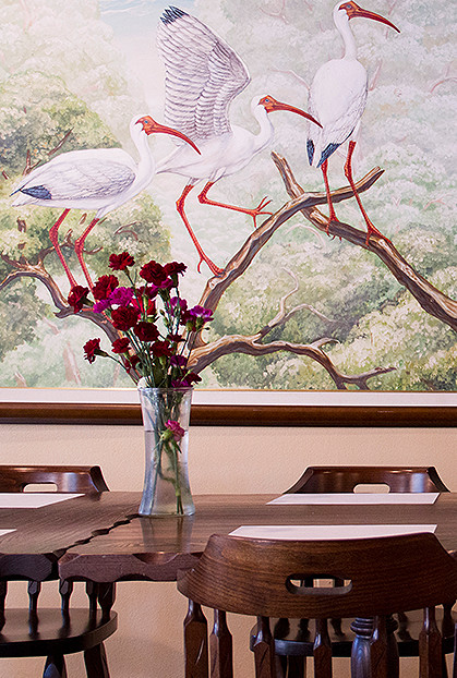 Painting of white birds on tree behind wooden table in dining area