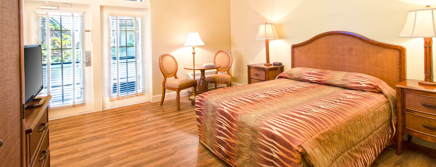 Room with king bed, wooden flooring, dresser & seating area next to window