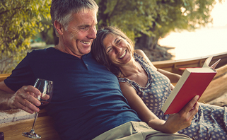 Older couple enjoying book while sitting on outdoor wooden bench