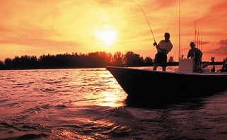 Silhouettes of two people fishing on boat with sun setting in the back