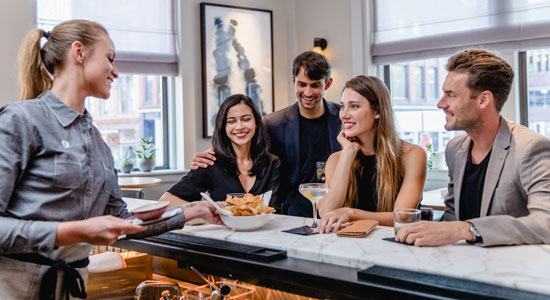 Waitress serving group of friends gathered at bar