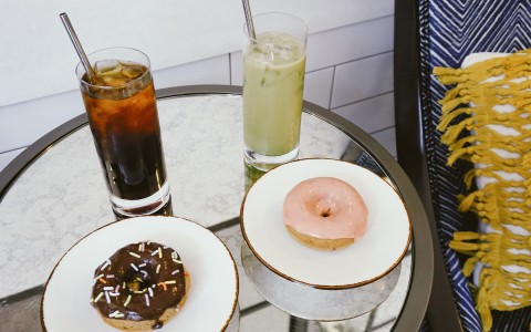 table with two icy  drinks and two small plates with donuts in them