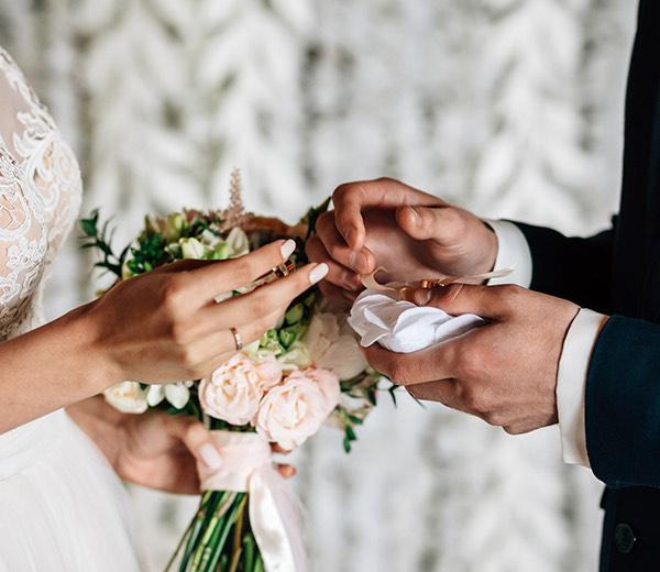 a couple of people holding flowers exchanging wedding bands