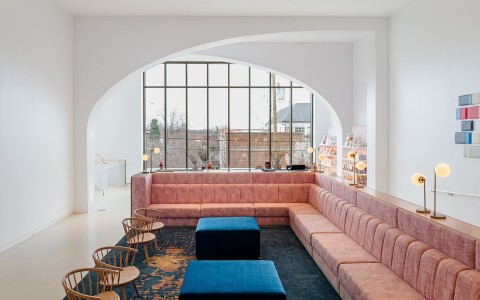Internal view of a social area with a large pink sofa and two blue tables 
