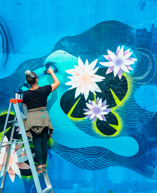 woman painting in a wall a blue mural 