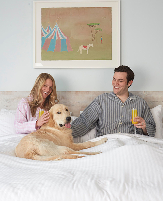 two couple sitting on a bed, and drinking mimosas