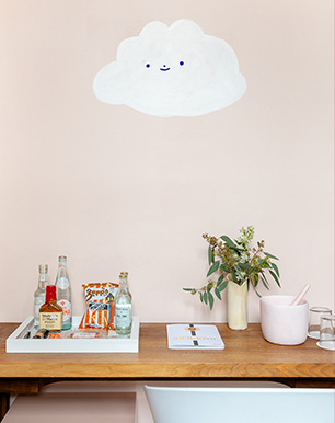 Desk with beverages and plant in the table and a white cloud painted in the wall 