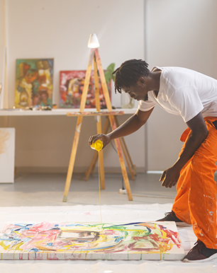 man with orange pants painting a big canvas