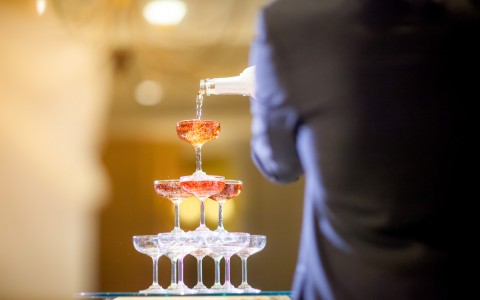 pouring champagne onto a pyramid made of champagne flutes