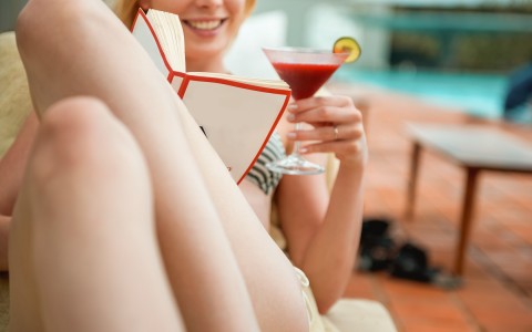 woman reading by the pool and having a cocktail