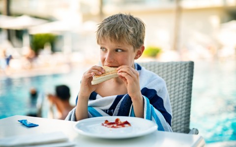 little boy eating a sandwich at the pool