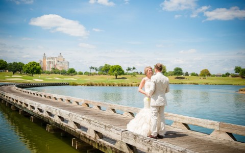 newlyweds standing on a long bridge with the hotel in the background