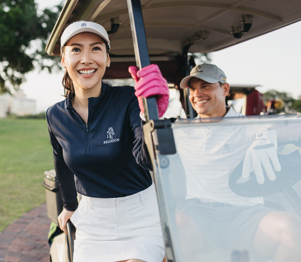 women smiling as she grabs onto the golf cart while man drives and smiles