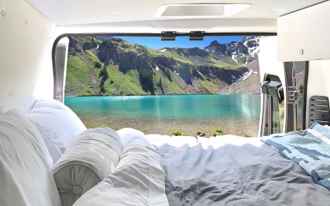 up-close bed view with a gorgeous bright blue lake in the distance, and big green mountains topped with snow