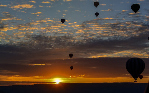 sun setting and multiple hot air balloons in the air