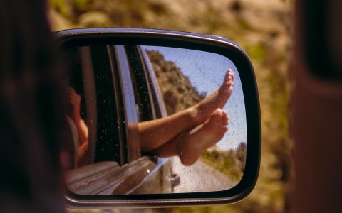 view in car mirror of bare feet sticking out of car