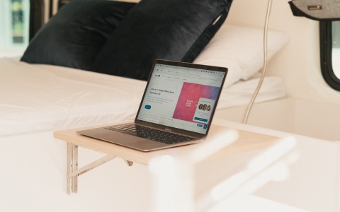 A laptop on a small table stand next to a bed