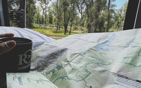 A large map with a hand holding a cup of coffee and trees in the back 