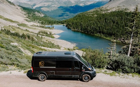 roameo van from the side. all black, black tored. trees and blue lake in the back next to mountains