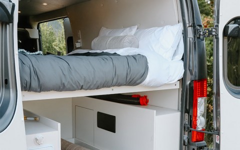 van opened from the back. shows the storage under the bed and the bed above 