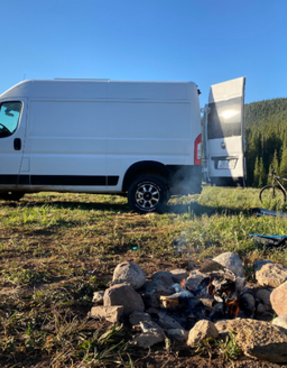 View of a firepit next to a white van and a bicycle on a field