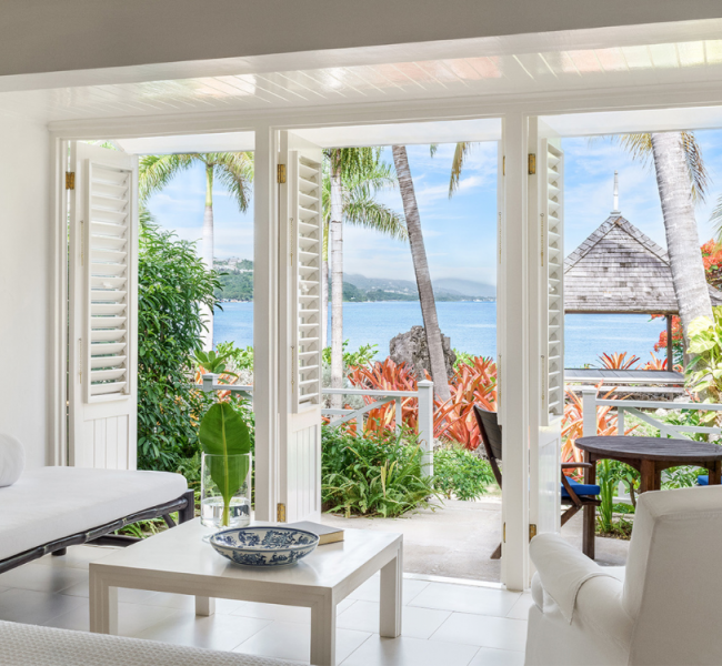 hotel room with all white furniture and doors open over looking the ocean