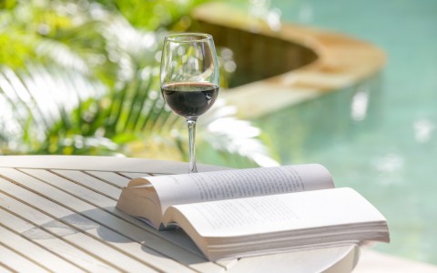 book and glass of wine on a table by the pool