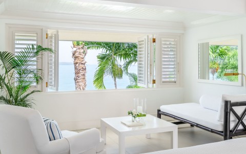 room window open to the ocean with white chairs by the window
