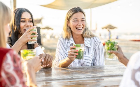 girls laughing and sipping on cocktails by the beach