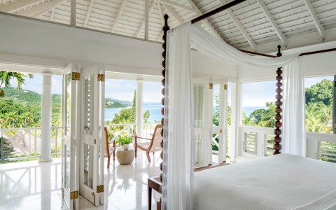 white bedroom with brown wooden bed posts and ocean view balcony