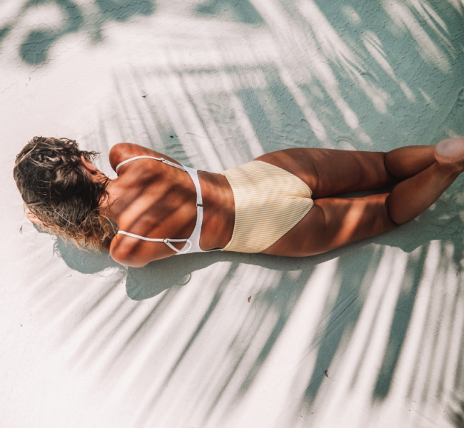 girl lying face down to the sand with palm tree shadow casting over her