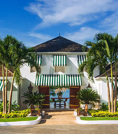 Front view of a big white hotel with palm trees and wonderful gardens 