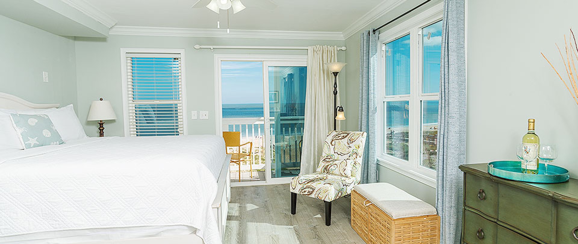 Room with king bed, dresser and chair next to window with ocean view (tablet version)
