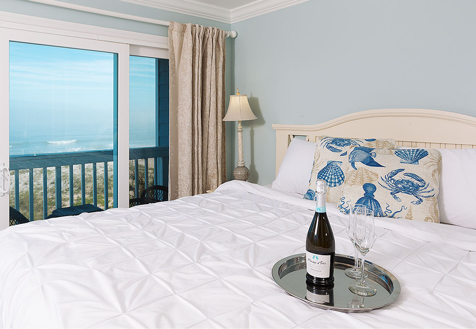 King bed with wine next to window with ocean view 