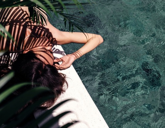 girl lying close to a pool and with a palm shadow on her body