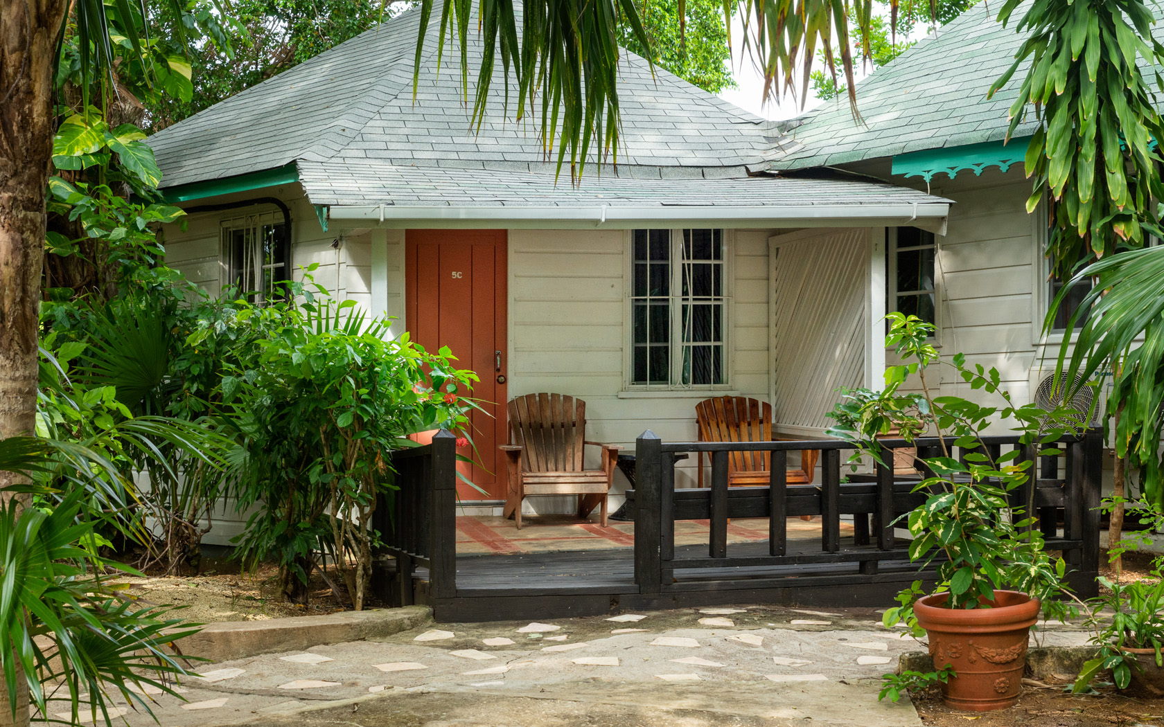 cozy adirondack chairs on front porch of bungalow surrounded by tropical trees 