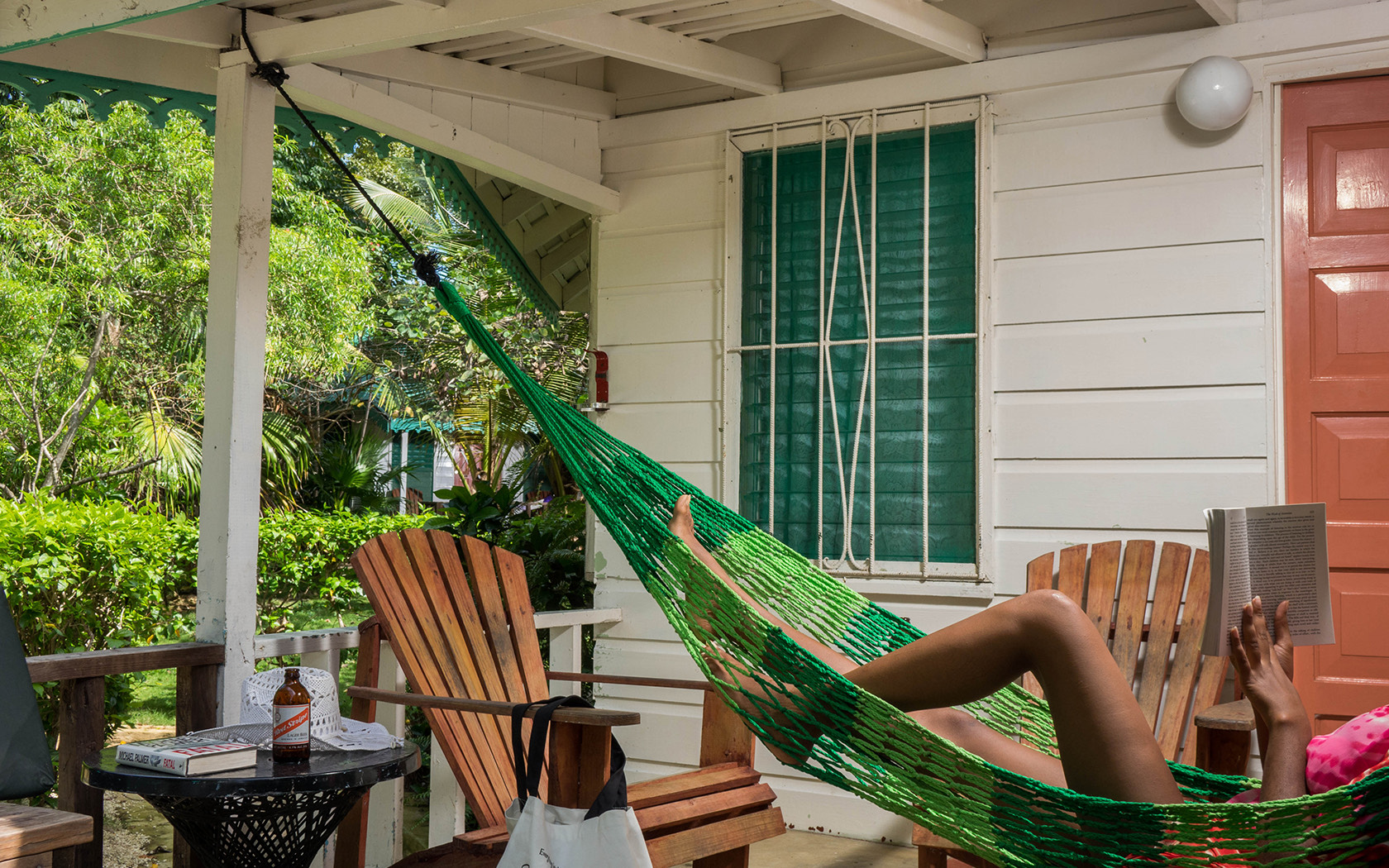 woman relaxing in a hammock reading a book in front of a bungalow