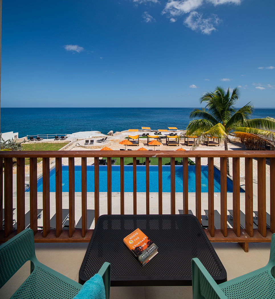 view from guest balcony overlooking pool and cabanas clear blue sky and deep turquoise waters